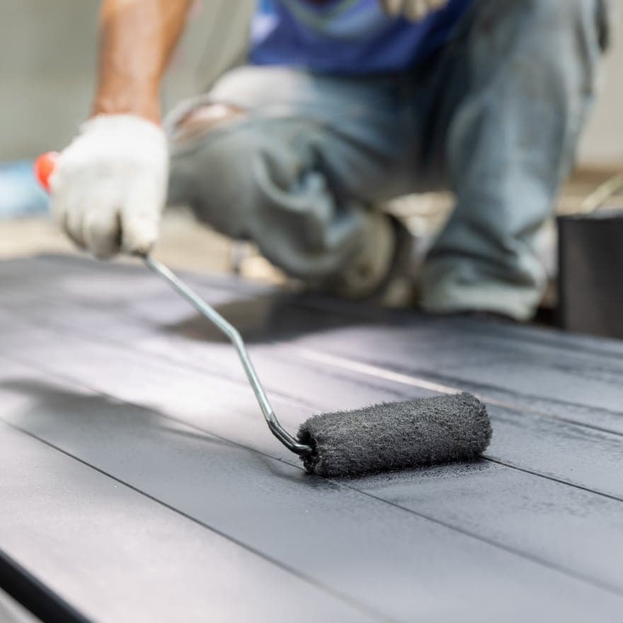 A roller laying grey paint along boarded decking